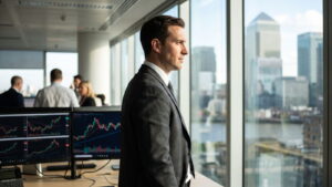 Trader in a suit in a glass office with Canary Wharf behind
