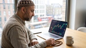 Trader at a desk with a trading platform, prayer beads and coffee