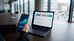 Trader reviewing a broker app on a phone beside a laptop